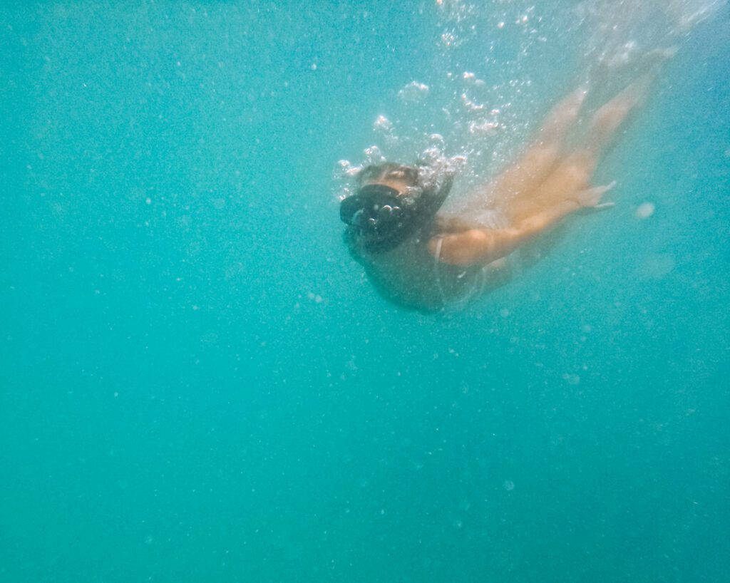 Girl in white bikini is swimming the the crystal clear light blue water in Thailand wearing a snorkle mask, diving below water surrounded by lots of airbobles in the ocean near Pig Island Koh Samui Thailand.